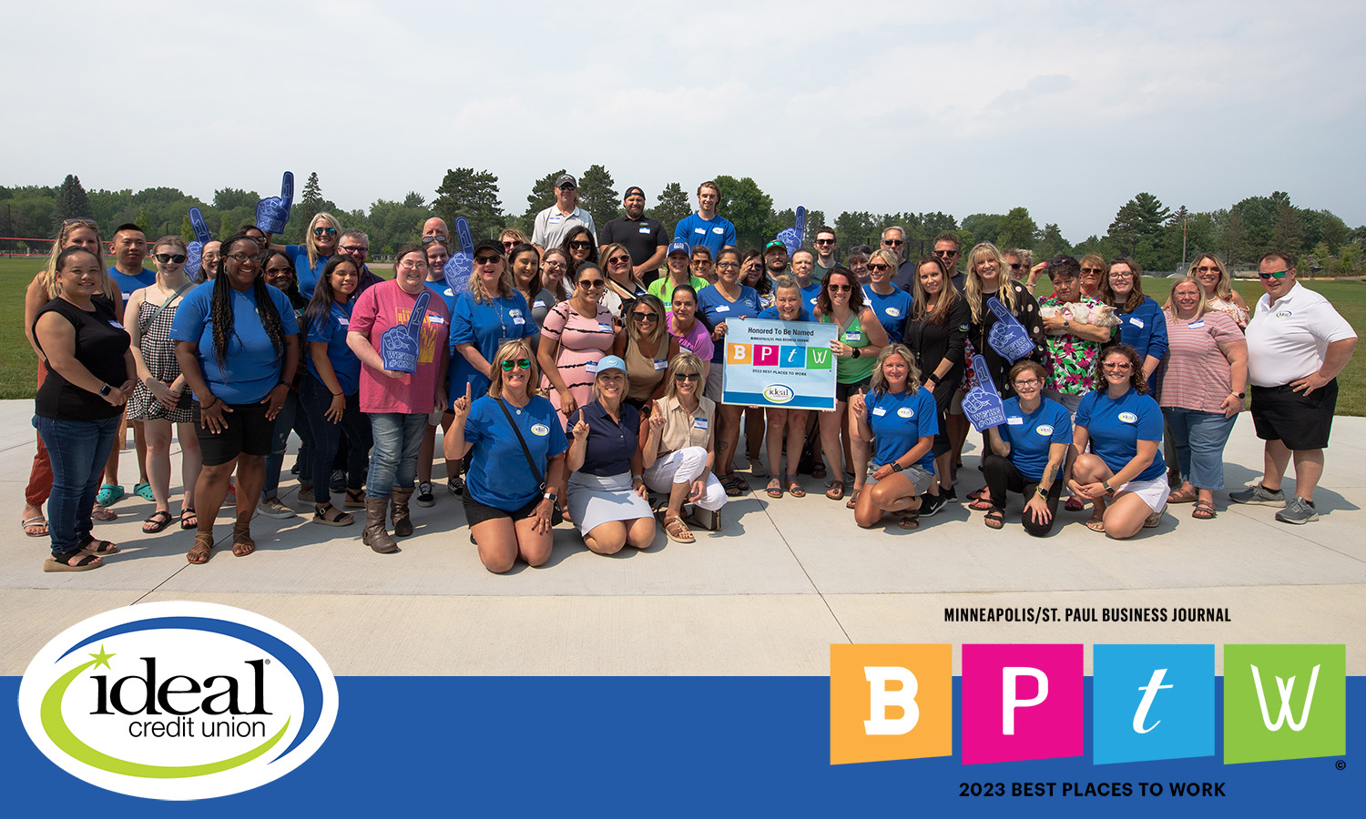 ideal cu staff standing outside with sign that says minneapolis/st paul bptw 2023 best places to work