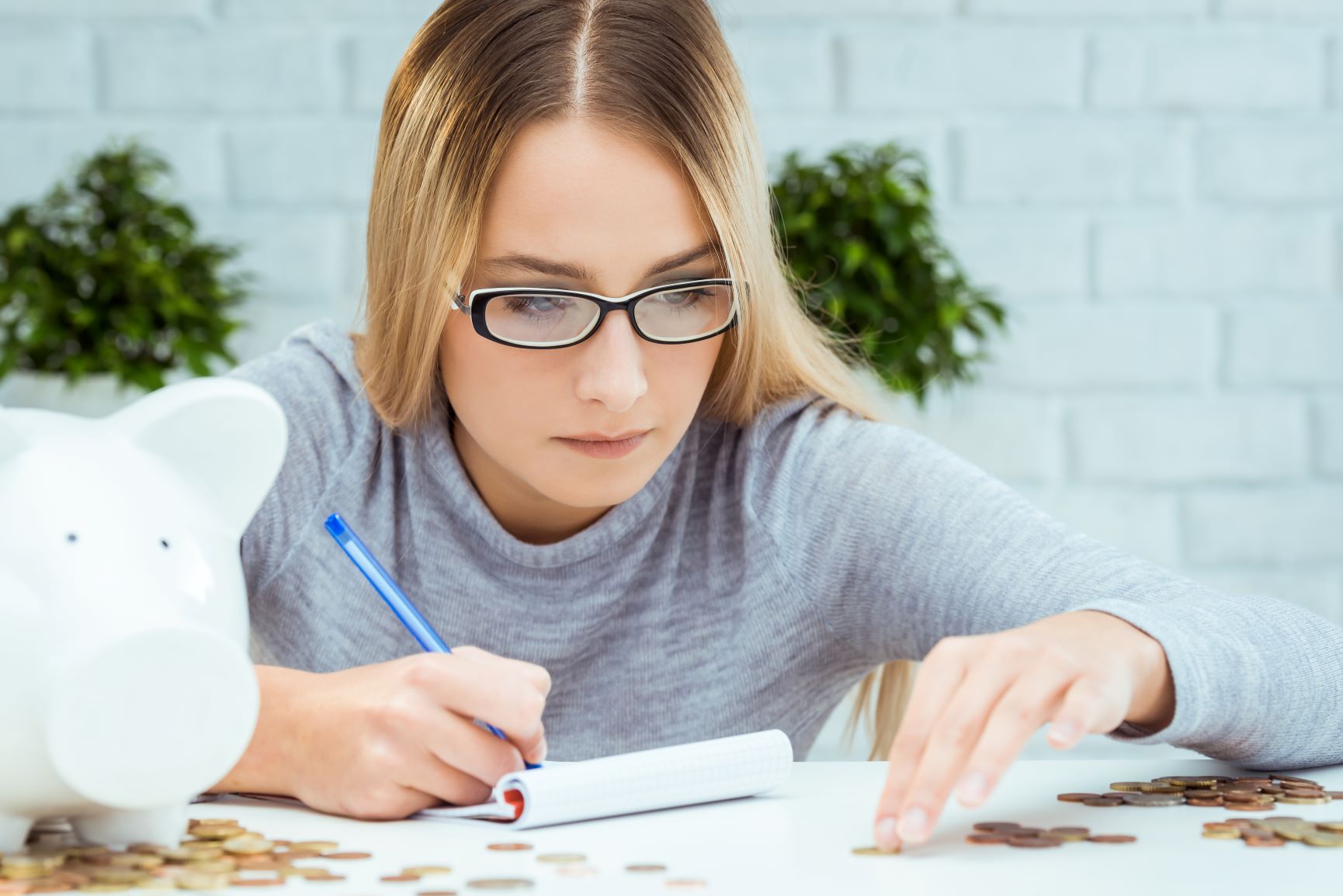 Young woman looking at coins and writing on a pad of paper