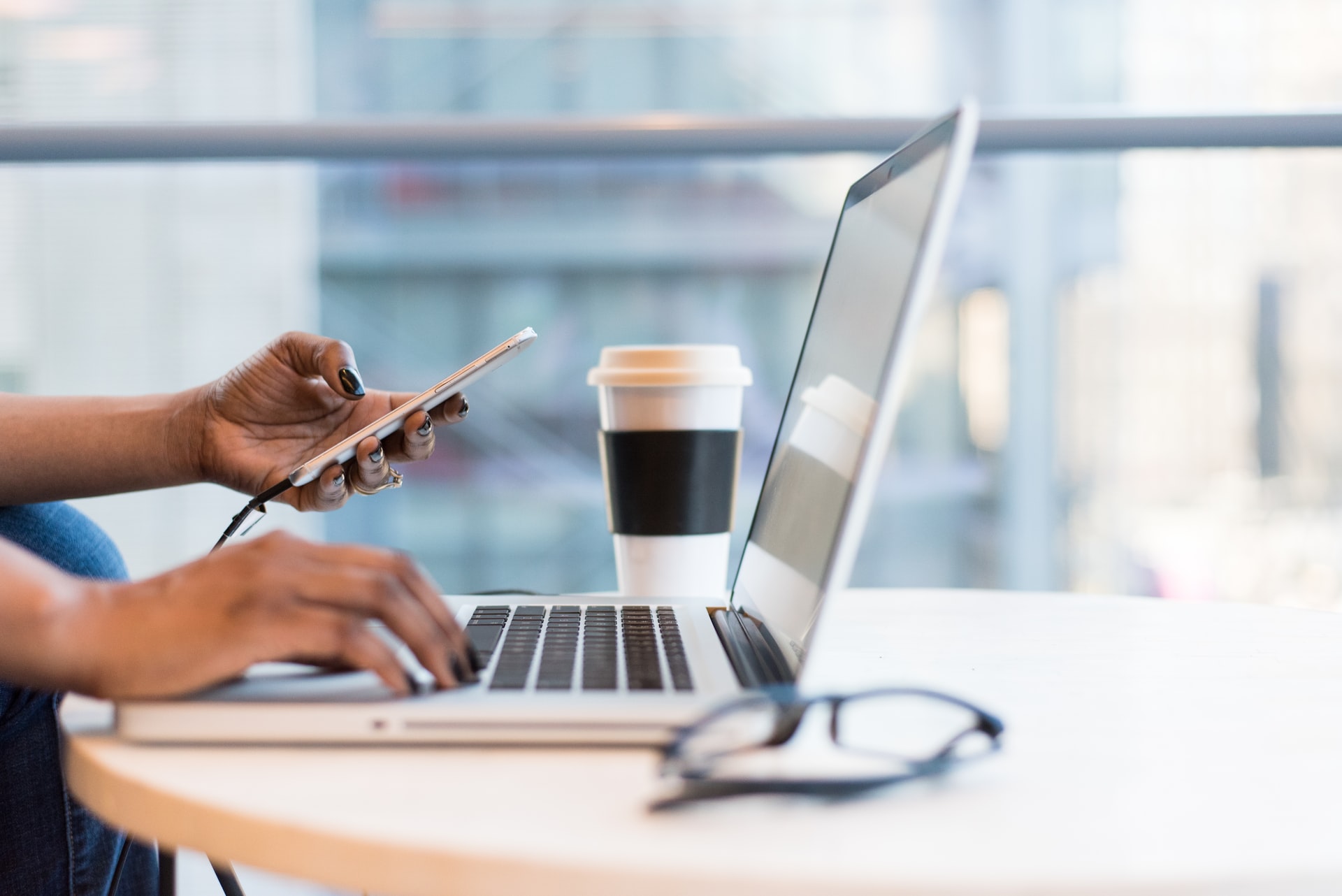 person sitting at laptop typing and holding cell phone