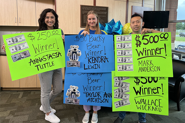 Three members of Ideal Staff with signs for winners of events, $250 Winner Annastasia Tuttle, $50 Bucky Bear Winner Kendra Lewin, $50 Bucky Bear Winner Taylor Ann Atchison, $500 Winner Mark Anderson and $500 winner Wallace Wickard
