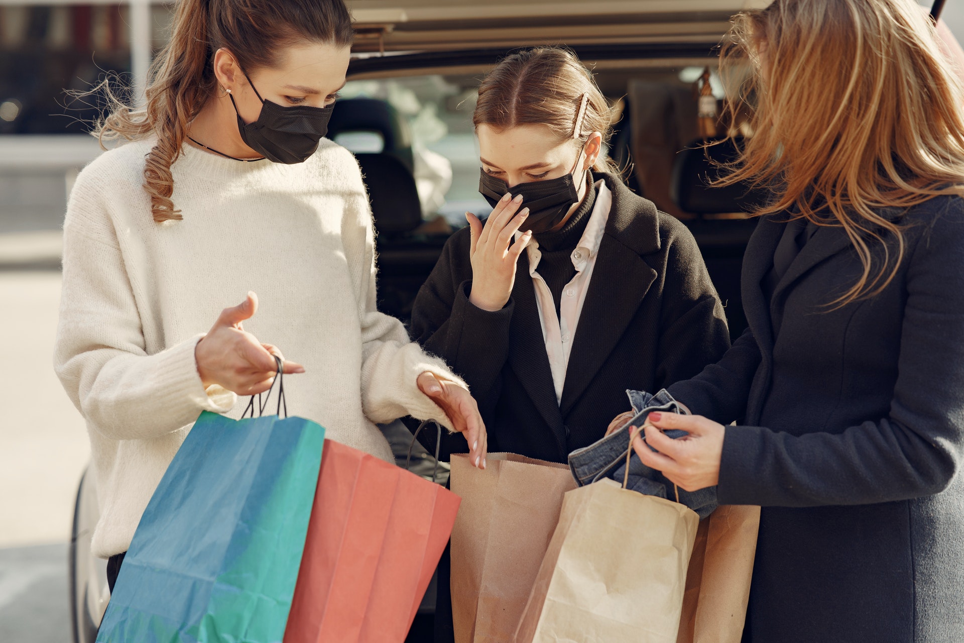 Three women wearing masks looking at shopping bags